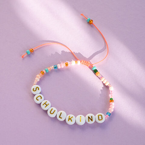 Perlenarmband Schulkind in orange/rosa und goldenen Buchstaben mit Säckchen in hellblau/weiss